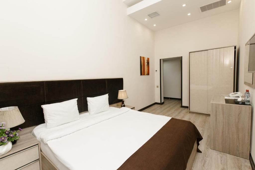 Une chambre d’hôtel moderne avec un grand lit, une table de chevet avec une lampe, une commode et un miroir.