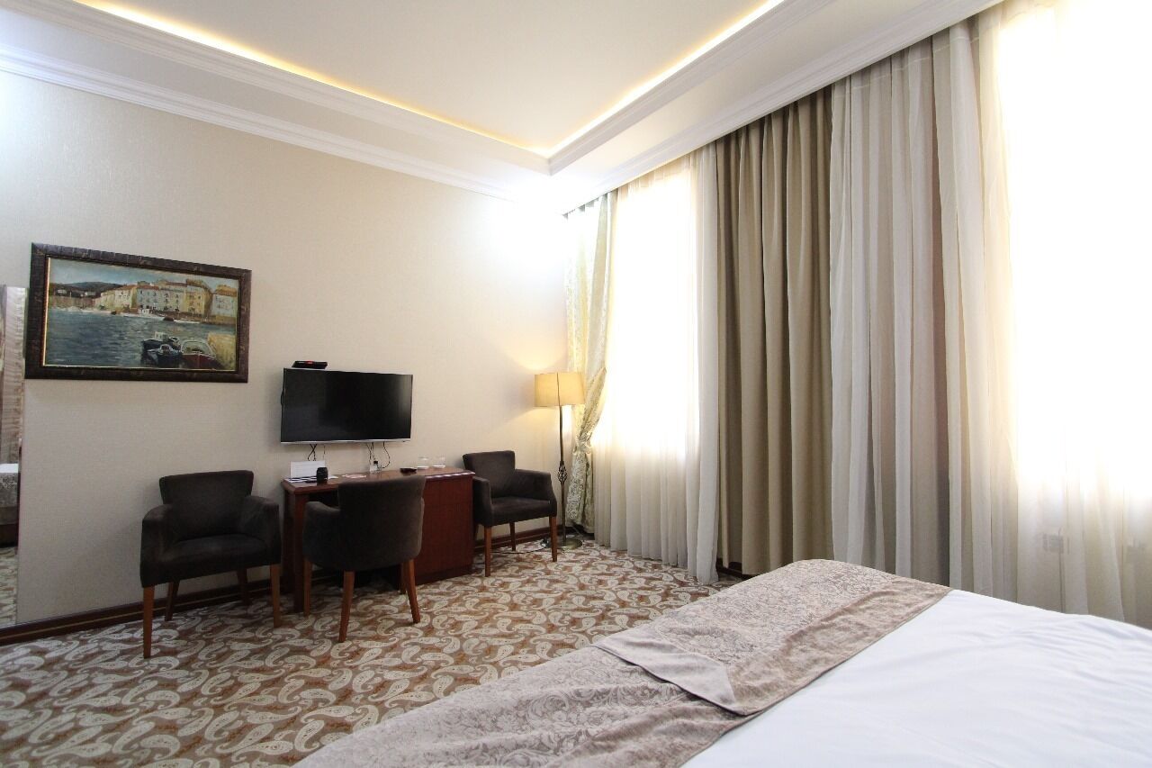 A hotel room with a bed, a desk, two chairs, a TV, and a painting on the wall.