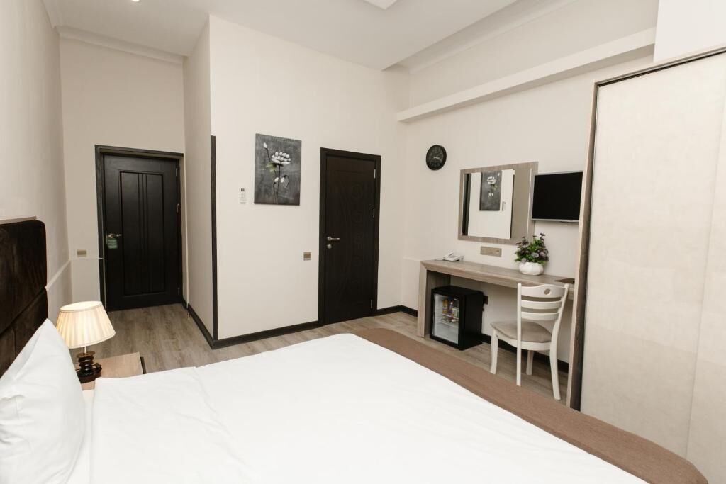 A hotel room with a bed, desk, chair, and a small refrigerator.