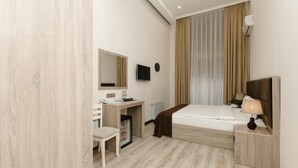 Ein modernes Hotelzimmer mit Bett, Nachttisch, Lampe und Schreibtisch mit Stuhl.