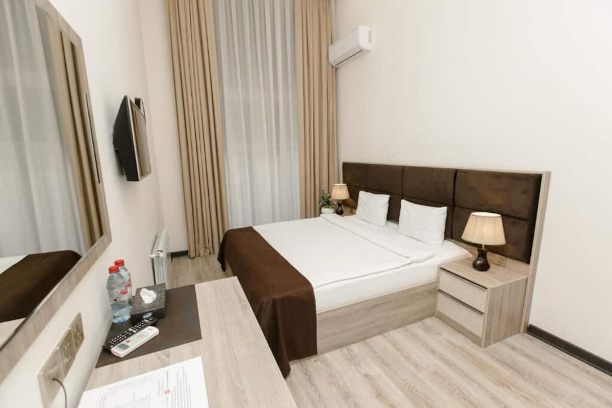 Une chambre d’hôtel comprenant un lit, des tables de chevet, un bureau, un miroir, une télévision et des rideaux.