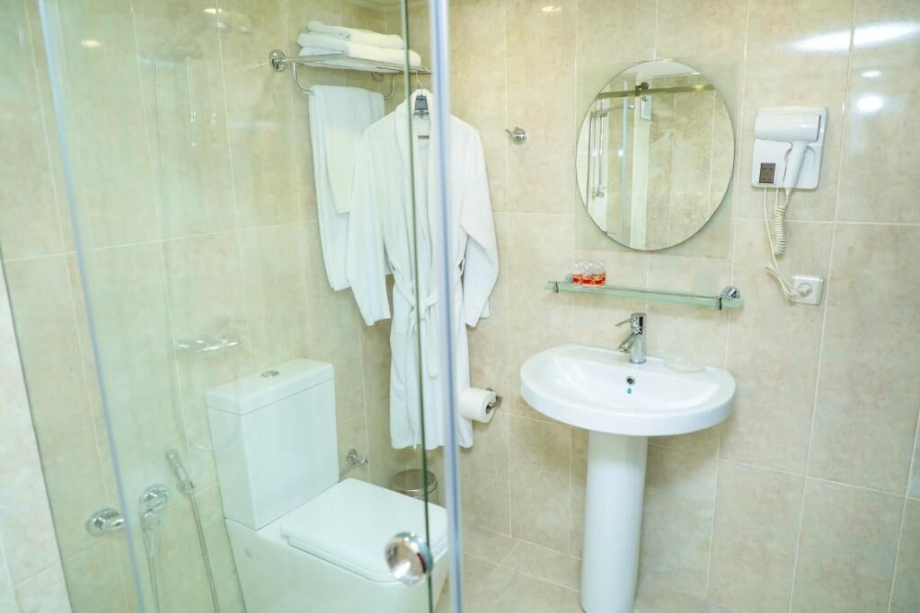 Een moderne badkamer met een glazen douchecabine, toilet, wastafel, spiegel en een haardroger aan de muur.