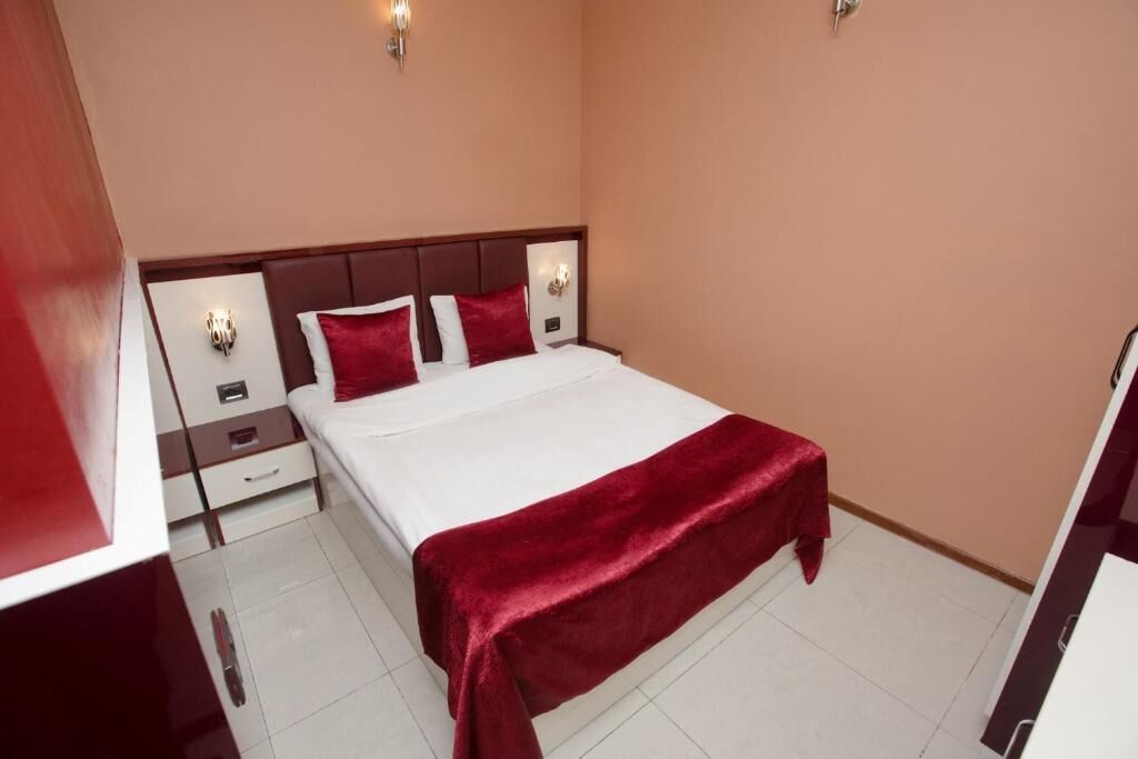 Habitación de hotel con cama, mesitas de noche y una manta roja.