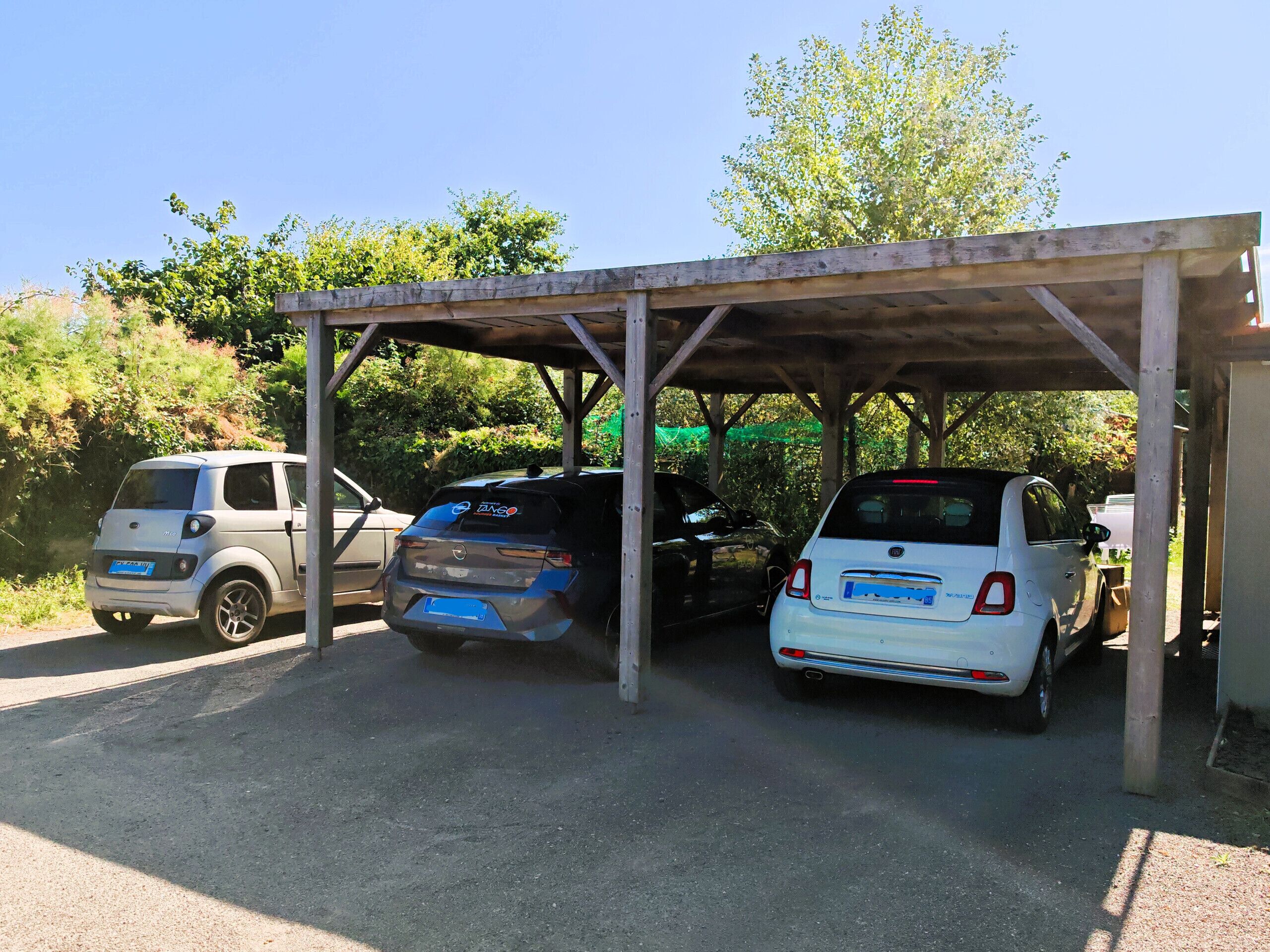 A covered parking area with three cars parked under a wooden structure.