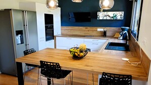 Une cuisine moderne avec une table en bois, des chaises noires et un panier de fruits.