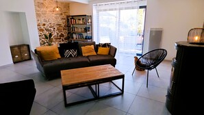 Un salon avec un mur en pierre, un canapé avec des coussins, une table basse en bois, une bibliothèque et une cheminée.