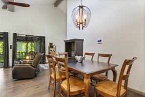 Ein Essbereich mit Holztisch und Stühlen, einer Chandelüster und Blick ins Freie durch große Fenster.
