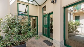 A building entrance with green-framed glass doors, a potted plant, and a metal grate on the ground. - Pink Loft by Wonderful Italy (Torino)