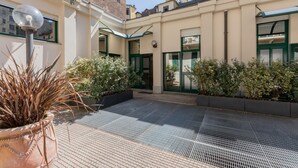 A courtyard with a tiled floor, potted plants, and a building with green-framed windows and doors. - Yellow Loft by Wonderful Italy (Torino)