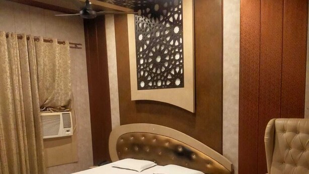 A hotel room with a bed, a chair, a table, and a decorative wall panel. - lvy Hotel And Restaurant (Mukerian)