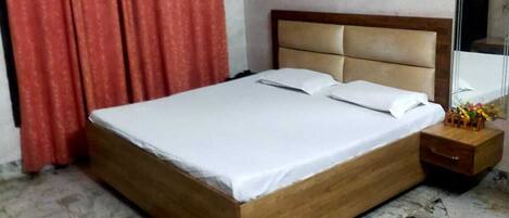 A hotel room with a wooden bed, red curtains, a floral wallpaper, and a marble floor.