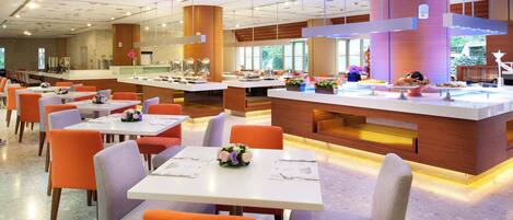 Um restaurante moderno com mesas brancas e cadeiras laranja, uma ilha central com displays de comida e grandes janelas que proporcionam luz natural.