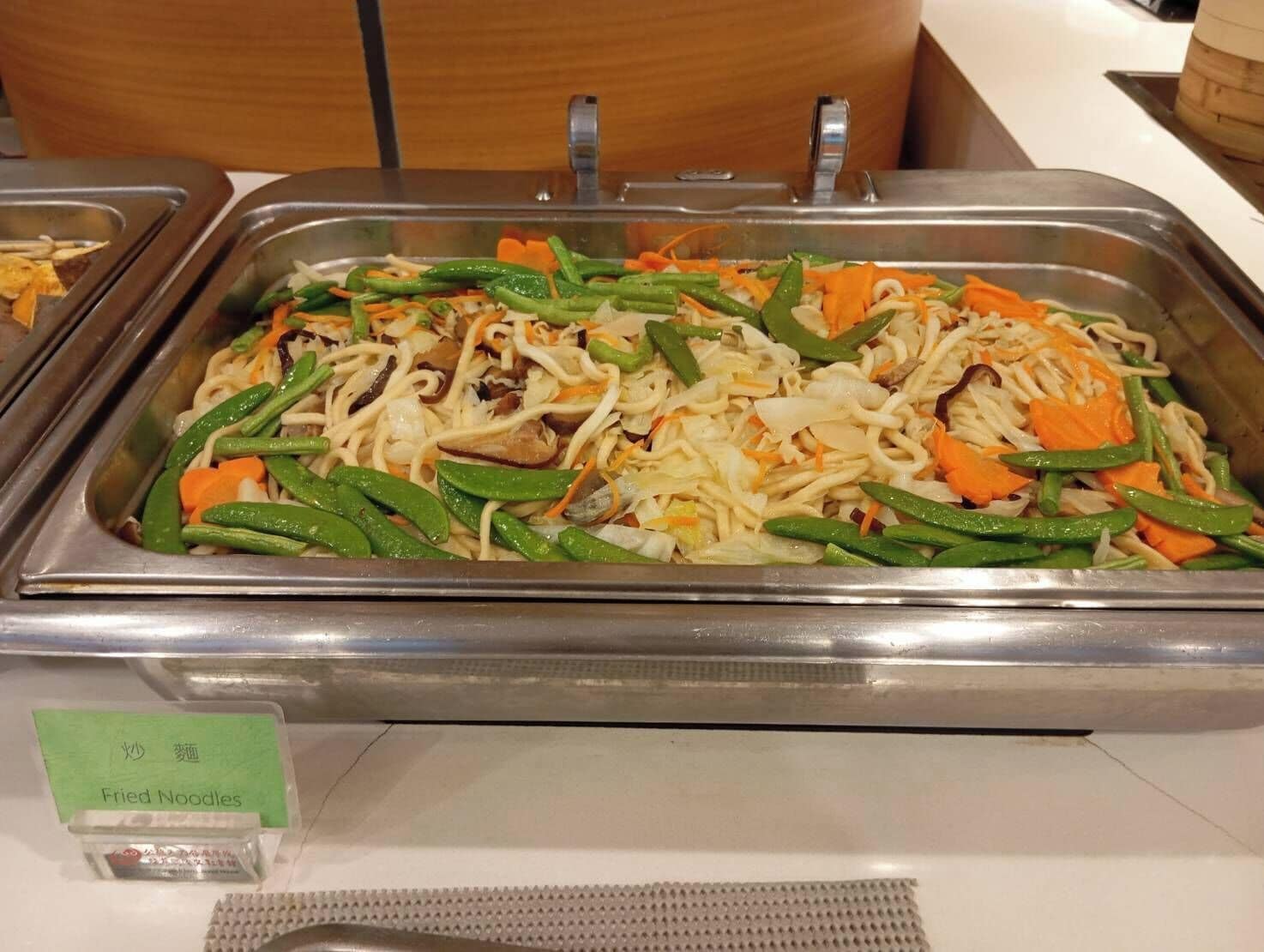 A buffet with a sign for 'Fried Noodles' and a variety of vegetables and noodles.