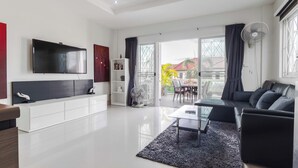 A modern living room with a flat-screen TV, white cabinetry, a black sofa, and a large window with curtains. - Sea View Near Beach  MuayThai C230 (Rawai)