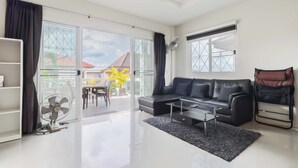 A modern living room with a black leather sofa, a glass coffee table, and a sliding glass door leading to a balcony. - Sea View Near Beach  MuayThai C230 (Rawai)