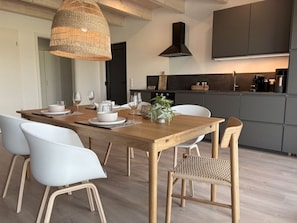 Una cucina moderna con mobili scuri, un tavolo da pranzo in legno, sedie bianche e una lampada a sospensione.