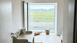A room with a large window, a wooden ceiling, a white bench, and a small table with a basket.