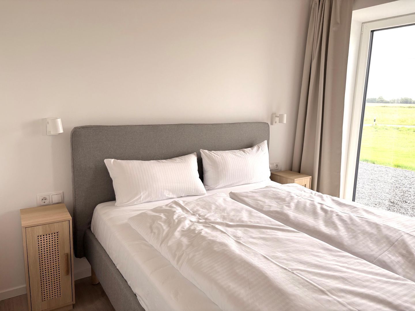A neatly made bed with white linens, a grey headboard, and two bedside tables with lamps.