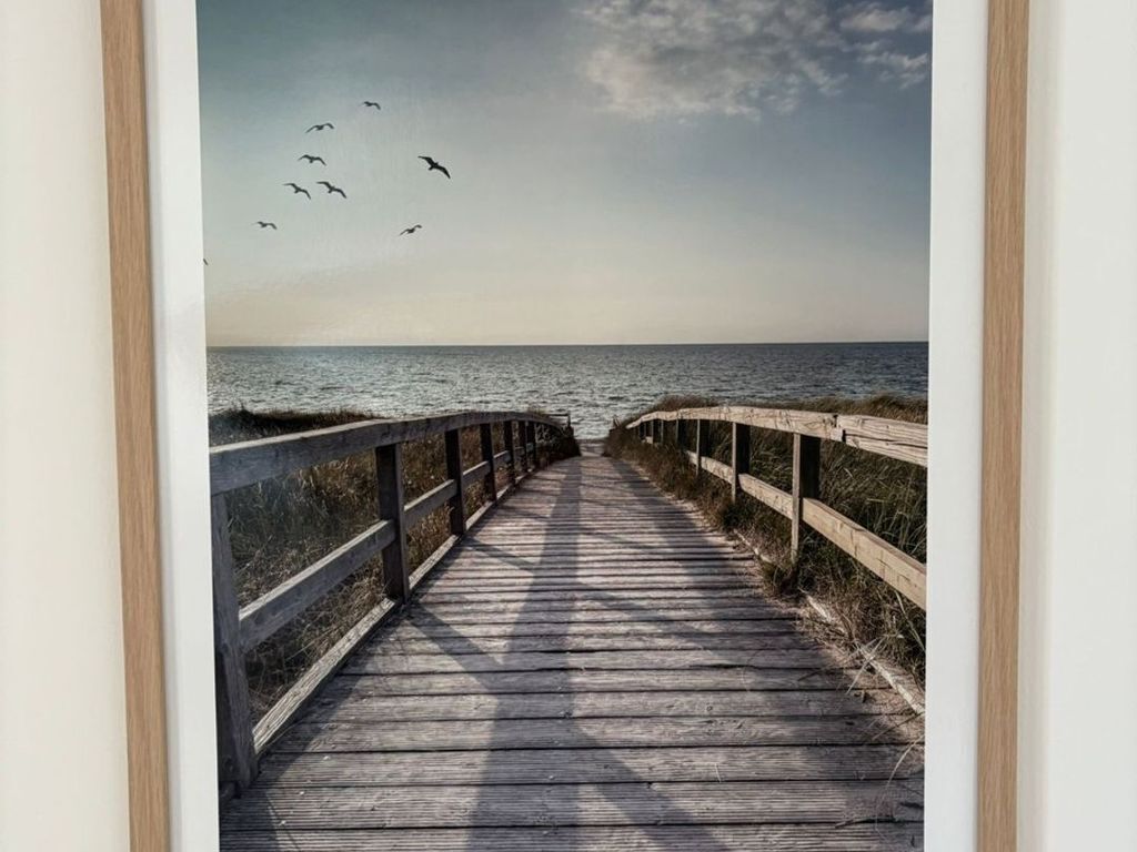 A wooden boardwalk leading to the sea with a railing on one side.