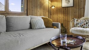 A cozy living room with a grey sofa, a round coffee table with a glass, and a wooden wall with a framed picture. - Val d'Illiez, 6 pers • Balcony & view - parking (Val-d`Illiez)