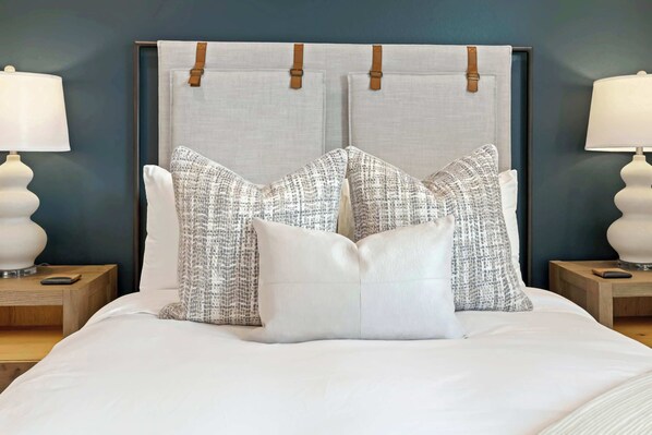 A neatly made bed with a headboard, two bedside lamps, and a nightstand with a remote control.