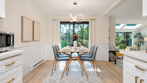 A modern dining area with a large window, a dining table set for four, and a kitchen with white cabinetry and a microwave.