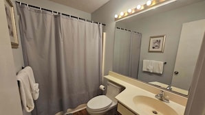 A bathroom with a shower curtain, toilet, sink, and mirror.
