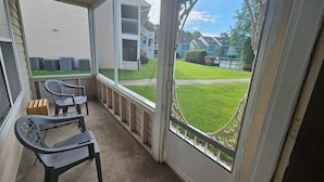 A covered porch with two chairs and a small table, overlooking a residential area with houses and a lawn.