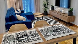 Un soggiorno moderno con un divano blu, un tavolo da pranzo con sottopiatti a motivi bianchi e neri e un televisore a schermo piatto montato a parete.