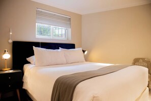 A neatly made bed with white linens, a dark headboard, and a bedside lamp on a nightstand.