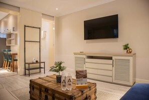 A modern hotel room with a wooden chest, a flat-screen TV, a plant, and a sign about Peru.