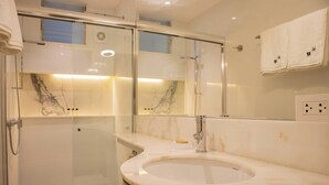 Une salle de bain dotée d’une douche à parois de verre, d’un meuble-lavabo recouvert de carreaux de marbre et d’un miroir au-dessus du lavabo.