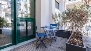 Un área de estar al aire libre con una mesa, sillas, una planta en maceta y la entrada de un edificio.
