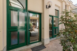 A building entrance with green-framed glass doors, a potted plant, and a small outdoor area with a bench and a table. - Green Loft by Wonderful Italy (Turin)