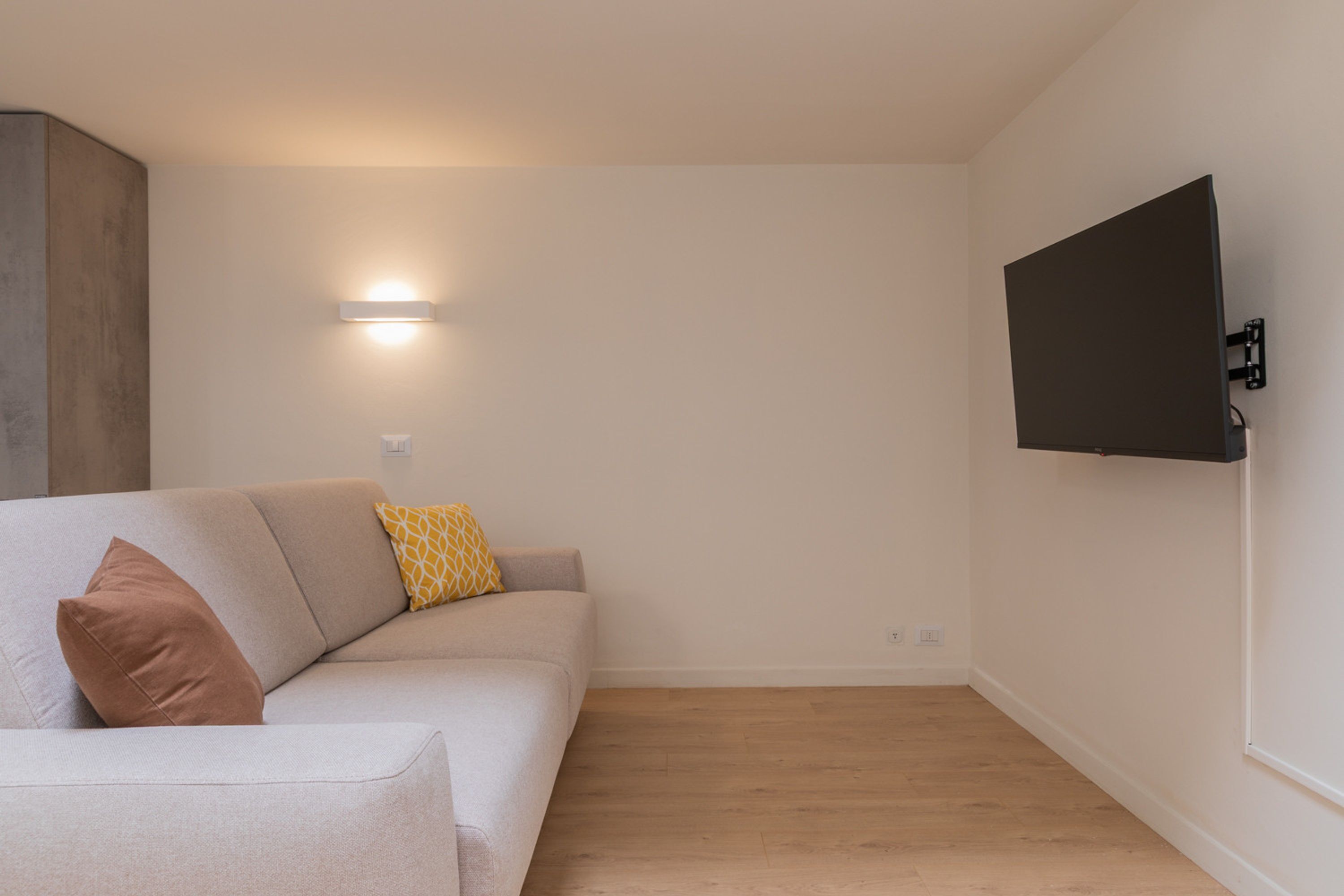 Un salon moderne avec un canapé de couleur claire, un téléviseur à écran plat fixé au mur et un luminaire fixé au mur.