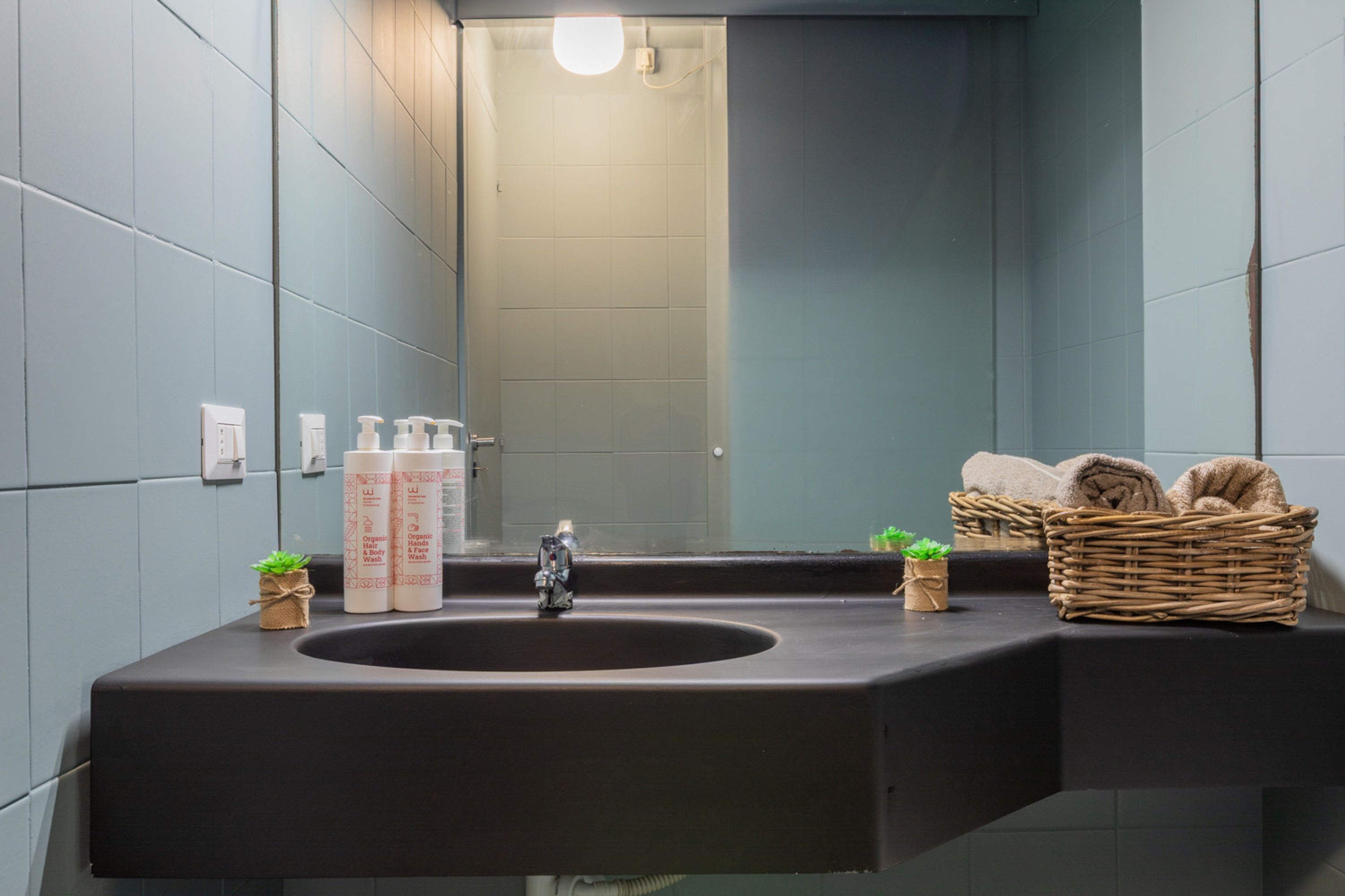 Een moderne badkamer met een zwarte wastafel, een spiegel en een rieten mand met handdoeken.