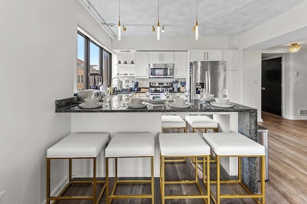 A modern kitchen with a central island, bar stools, stainless steel appliances, and a large window.