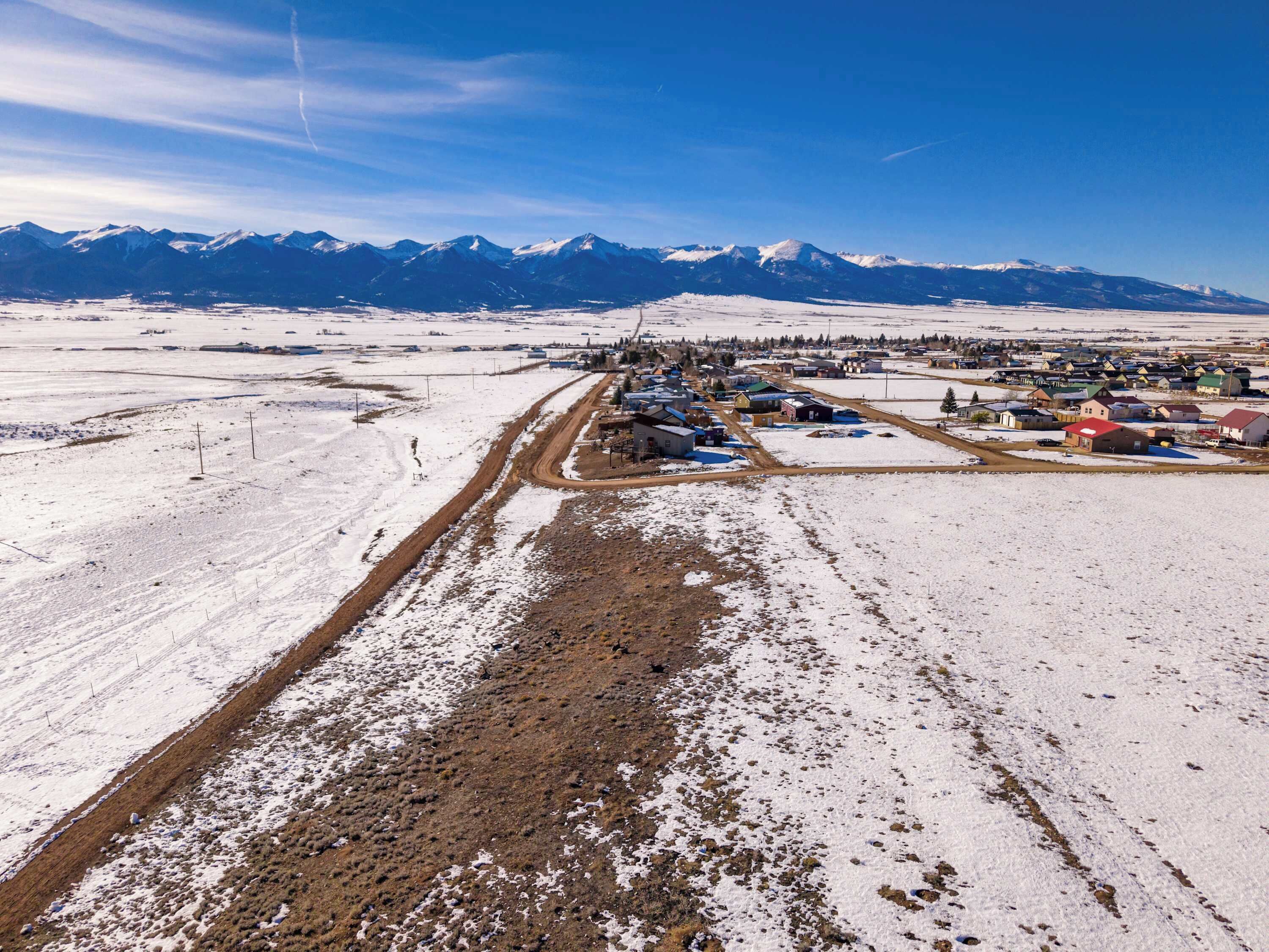 A snow-covered landscape with a small settlement and a mountain range in the background.