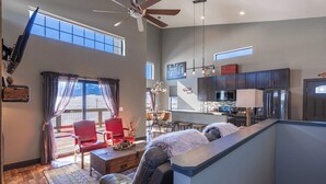 A spacious living area with a large window, a ceiling fan, and a modern kitchen in the background. - Epic Mountain View Dark Skies Retreat with 2 Living Spaces, Perfect for Couples & Families (Silver Cliff)