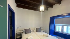 Une chambre avec deux lits, une fenêtre ornée d’un cadre bleu, un lustre et un bureau avec une lampe.