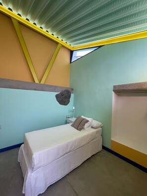 Una habitación pequeña con cama individual, techo inclinado y tragaluz.