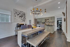 A modern kitchen with a central island, a dining area with a long table and benches, and a large abstract painting on the wall. - Stylish 2BR Inman Park Flat w/ Porch & Fireplace (Atlanta)