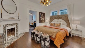 A bedroom with a fireplace, a large bed with an ornate headboard, a chandelier, and a view of the outdoors. - Stylish 2BR Inman Park Flat w/ Porch & Fireplace (Atlanta)