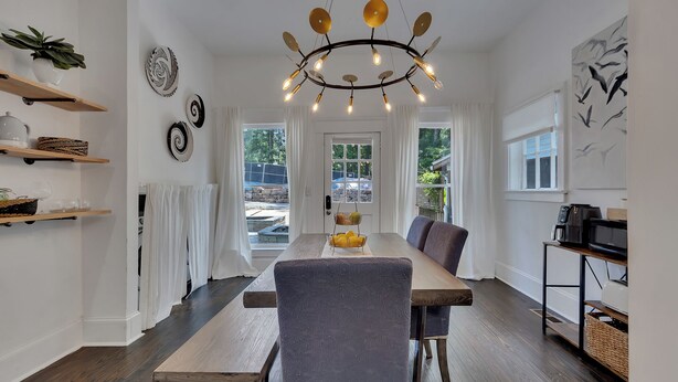 A modern dining area with a wooden table, grey upholstered chairs, and a unique chandelier. - Stylish 2BR Inman Park Flat w/ Porch & Fireplace (Atlanta)