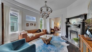 A spacious living room with a modern chandelier, a blue sofa, a glass coffee table, and a fireplace. - Stylish 2BR Inman Park Flat w/ Porch & Fireplace (Atlanta)