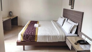A modern hotel room with a large bed, bedside table, and a desk with a chair. - Hotel Dwarika Inn (Rajkot)