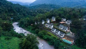 Un resort en una ladera con varias edificaciones blancas, una piscina y un río que atraviesa el paisaje.