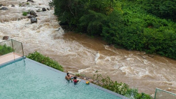 Una piscina con vistas a un río caudaloso y abundante vegetación.