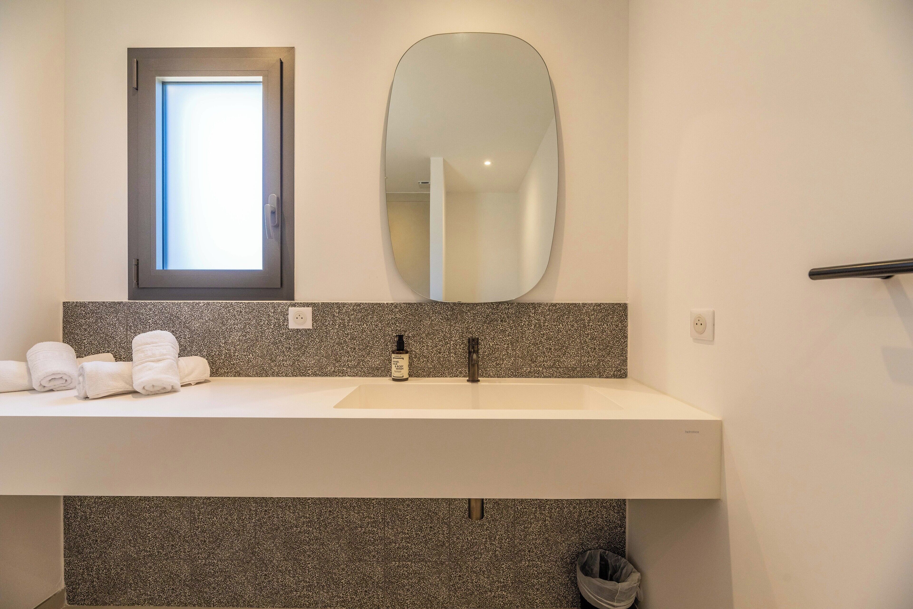 Un baño con un lavabo blanco, un espejo grande, una ventana sobre el lavabo y toallas en la encimera.