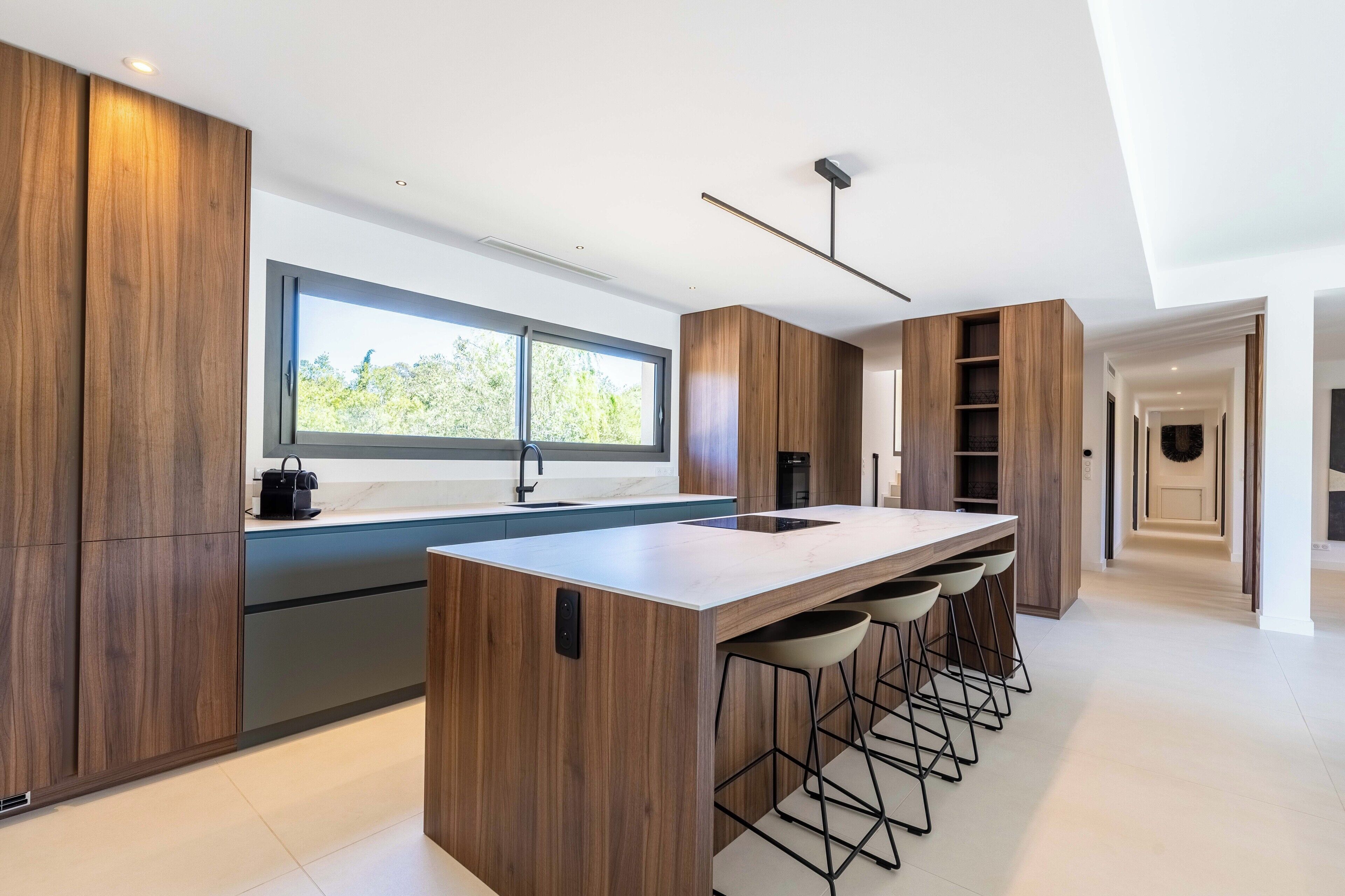 Een moderne keuken met een groot kookeiland, barstoelen en een raam.